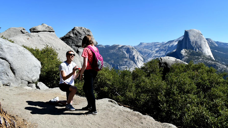 Daniel pictured on one knee as he proposes to Sarah against a backdrop of mountains
